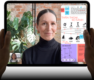 iPad Pro, vỏ ngoài mặt trước, nằm ngang, màu đen không gian, các góc bo tròn, viền màn hình màu đen, bàn tay cầm ở bên trái và bên phải, màn hình hiển thị cuộc trò chuyện FaceTime đang được dịch trực tiếp, và một ứng dụng giáo dục hiển thị bài thuyết trình "Thần Thoại So Sánh" với văn bản, biểu đồ và ghi chú viết tay